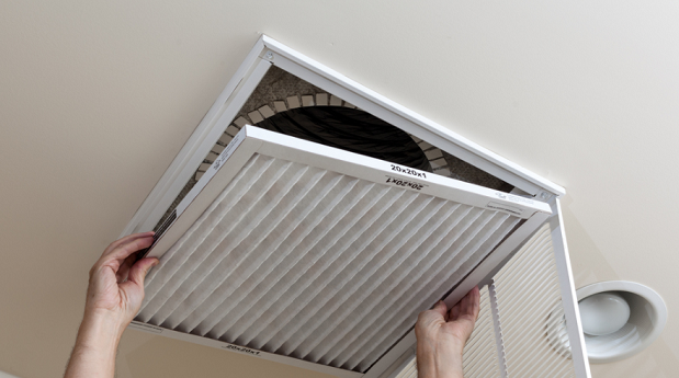 A pair of hands reaching out and removing air filter from return on ceiling.