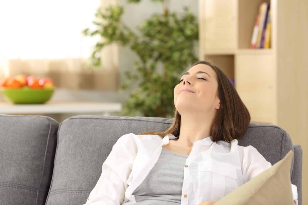 Woman relaxing on gray couch, enjoying fresh indoor air.