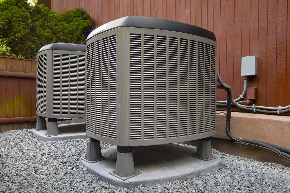 Two HVAC units outside a home with vertical woodgrain siding.