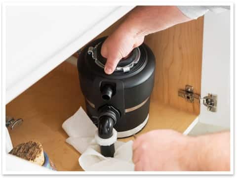 Technician servicing a garbage disposal under a sink.
