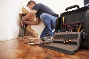 Male plumber repairing leak in wall, focus on foreground